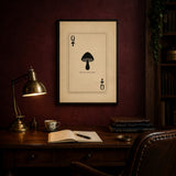 Queen of Spores print framed in black above a walnut writing desk with a notebook and brass lamp, shown in 50x70cm